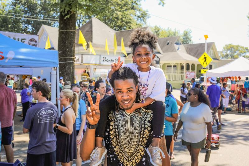 man with young girl on shoulders both hold up peace signs at Cooper young festival