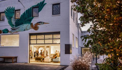 People inside the gallery space at Ugly Art Co with a large blueish-green bird mural above the entrance.