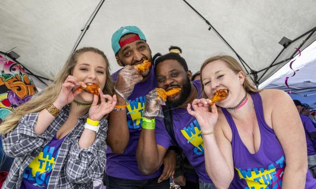 People eating chicken wings in a tent at a festival.