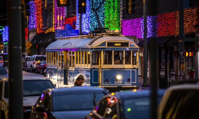 blue trolley going down street during Christmas time with lights in background