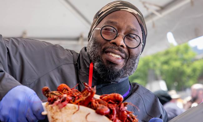 A man holds up scoop of crawfish and smiles for photo.